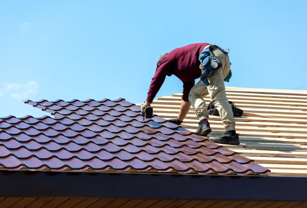 roofer using nail gun to install metal tiles on house roof