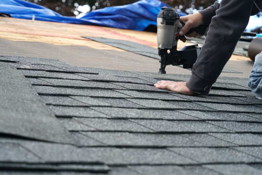 A worker is replacing the damaged shingles on roof