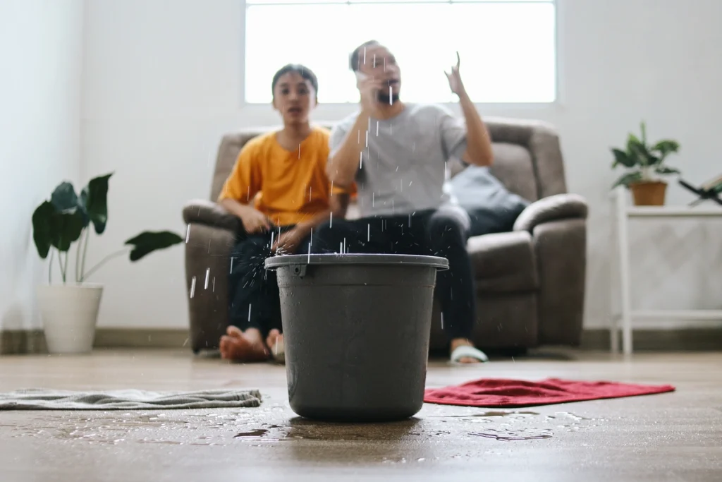 roof leak repair cost-family sitting on the couch while a bucket catches dripping water from ceiling