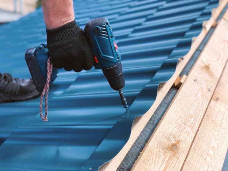 metal roof installation mistakes-close up image of a gloved hand using power tools to install metal roofing materials