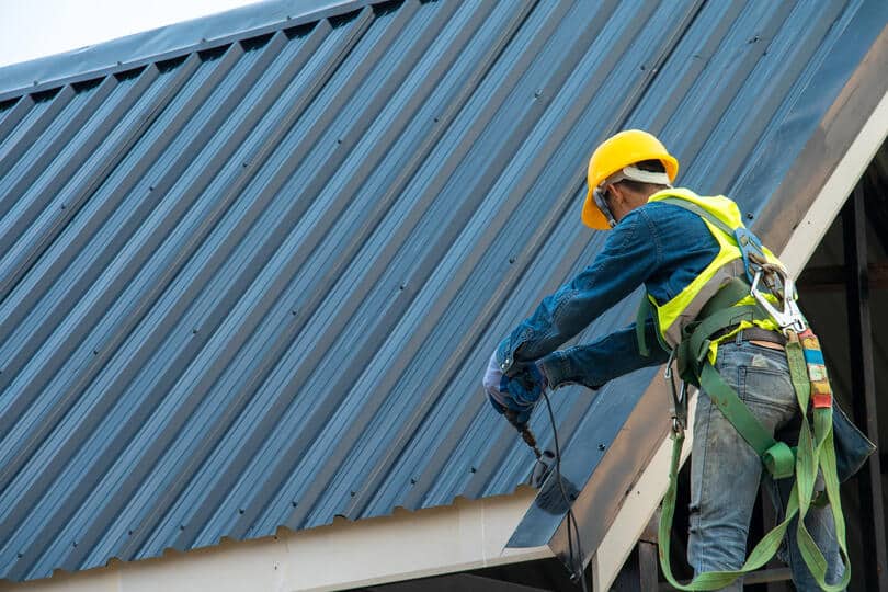 metal roof installation mistakes-roof tech standing on a ladder using power tools to install metal roofing materials